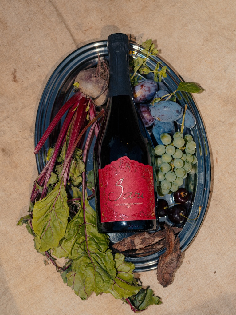 Bottle of Sari Red with a crimson label on a plate with grapes, beetroot, plums and dark fruit
