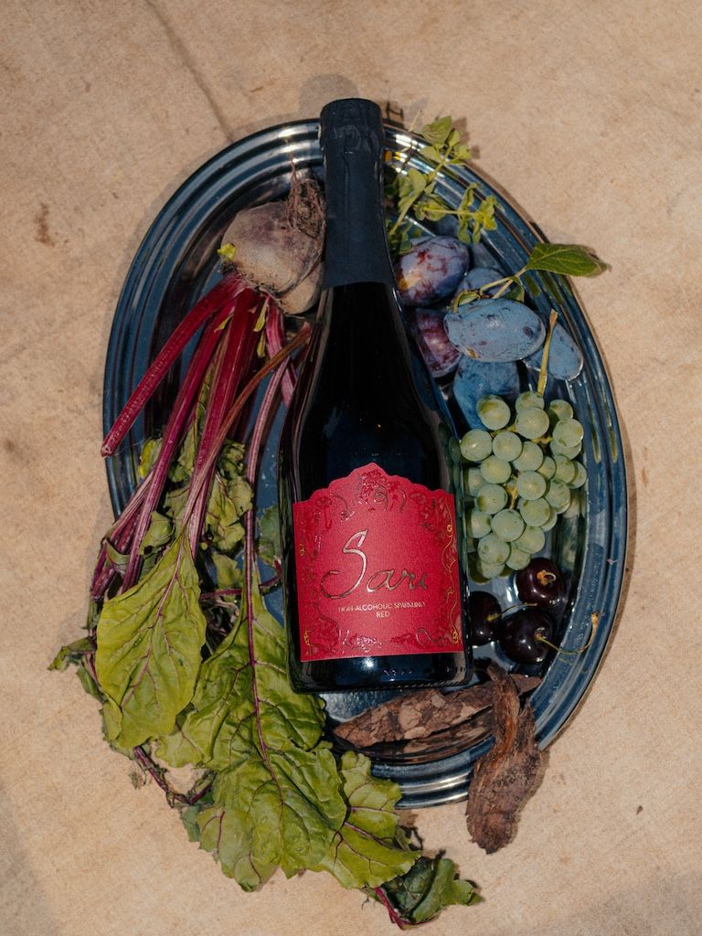 Bottle of Sari Red on a silver tray with plums, grapes, cherries and beetroot