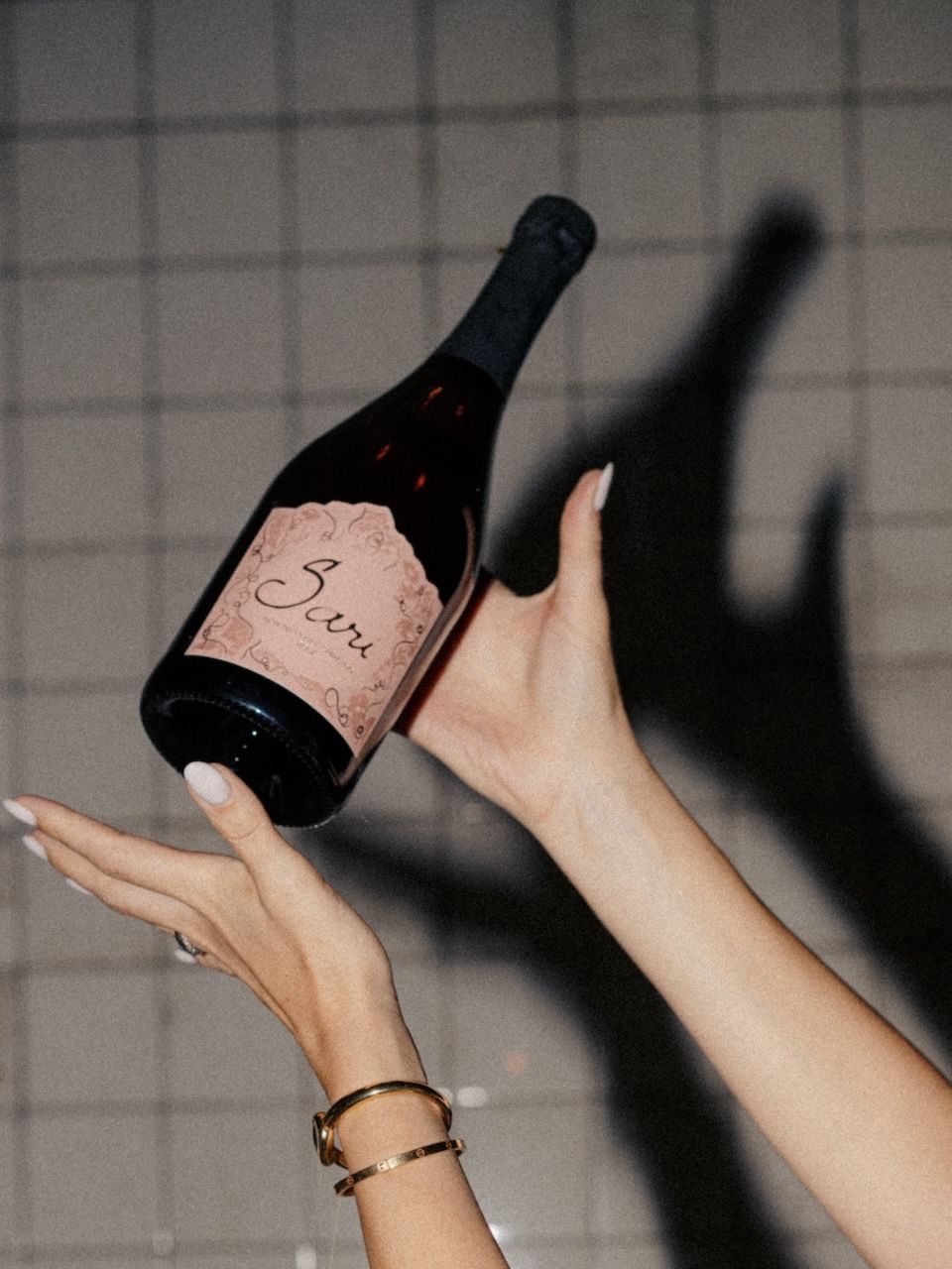 Hands holding a bottle of Sari Rosé against a tiled wall with a soft shadow