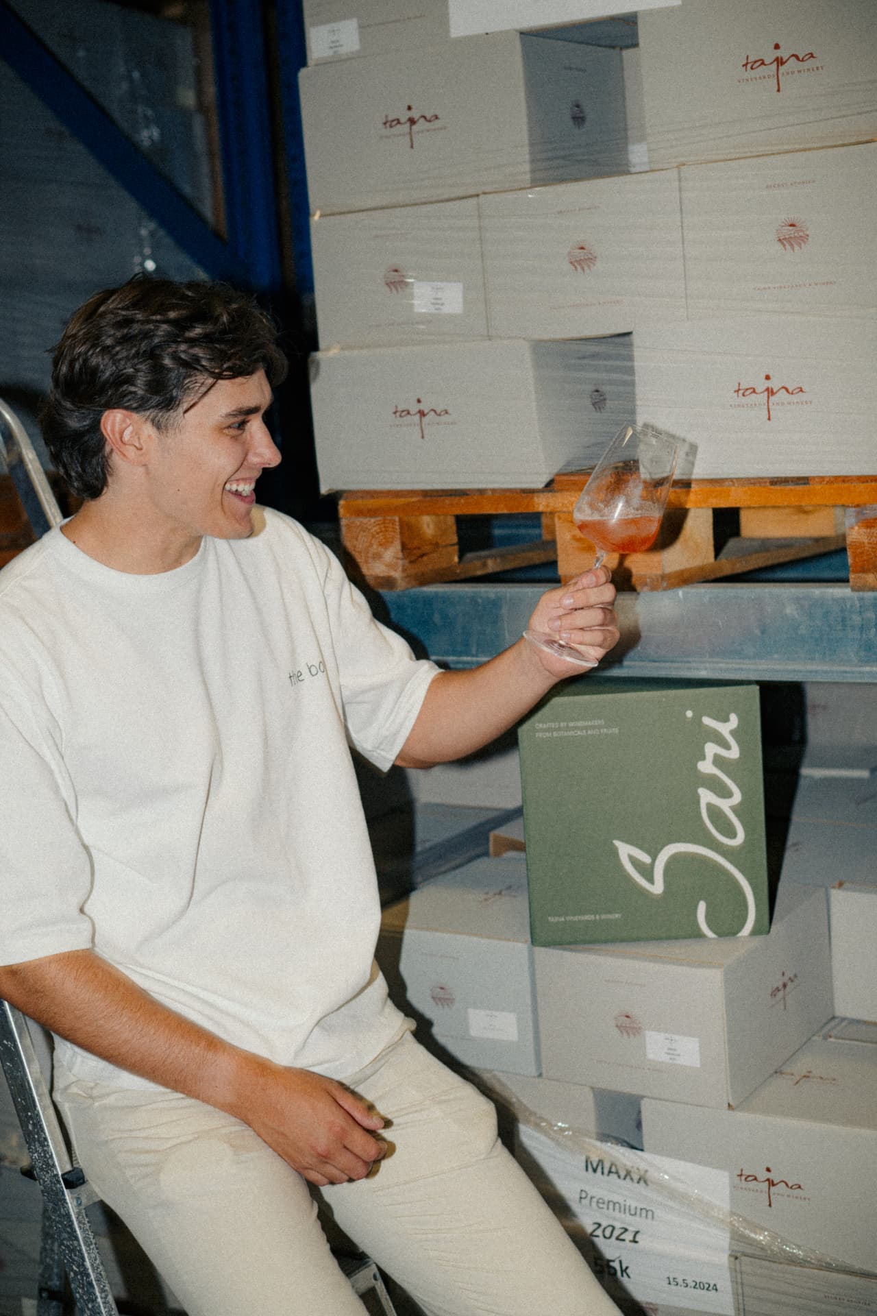 Man raising a glass of Sari beside stacked Sari boxes in the warehouse