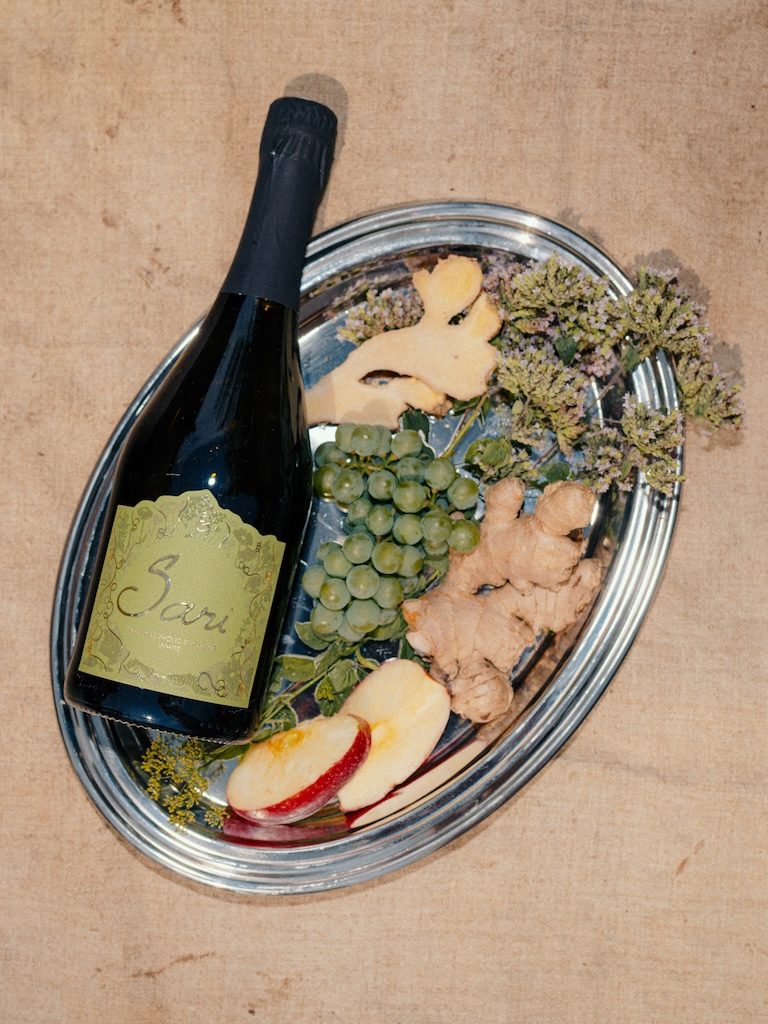 Bottle of Sari White on a silver tray with grapes, apple, ginger and dried flowers