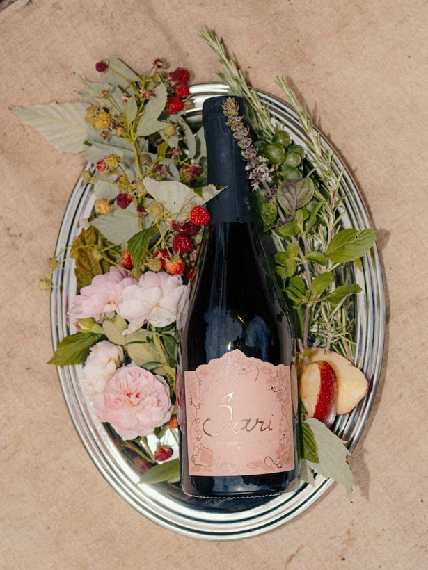 Bottle of Sari Rosé laid on a plate with raspberries, rhubarb and fresh herbs