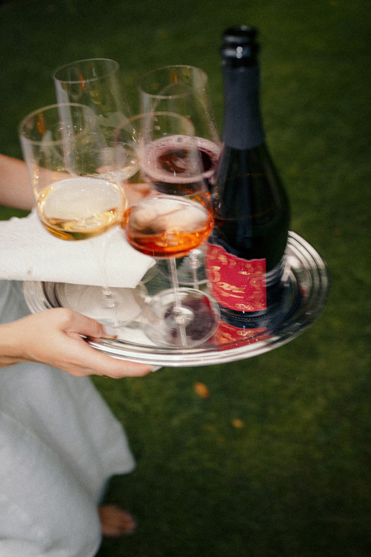 Hands carrying a silver tray with glasses of Sari White, Rosé and Red and a bottle
